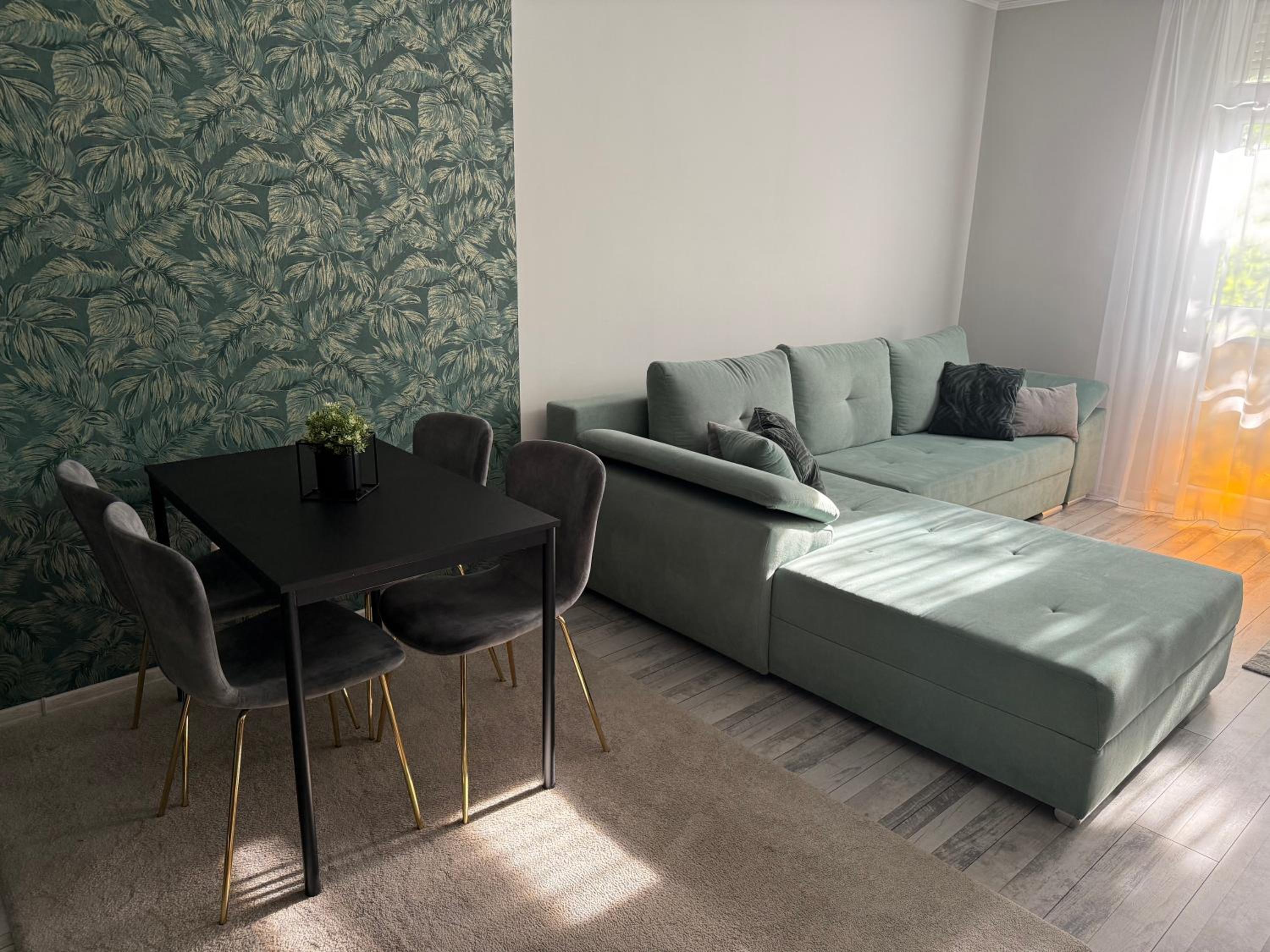 Boulevard Apartman – Nappali zöld sarokkanapéval és étkezőasztallal